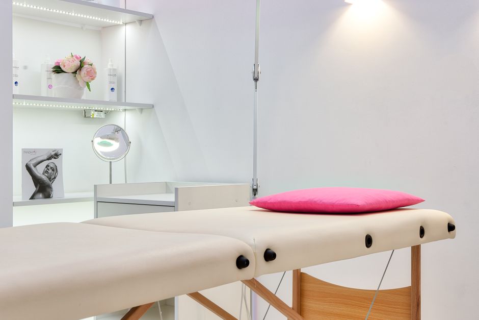 A bright, quiet treatment room with a treatment bed and a small shelf of products