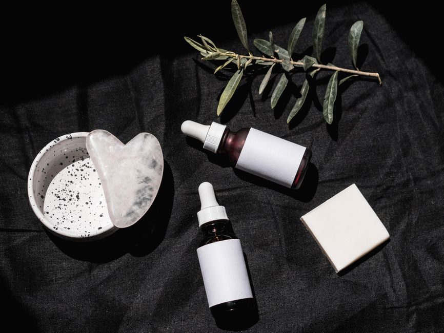 Dropper bottles of face serum on a dark cloth beside a gua sha stone
