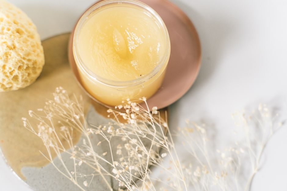 An open jar of facial scrub beside a natural sponge